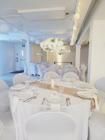 Salle polyvalente Espace Franny dressée en blanc, table ronde nappée et centre de table fleuri