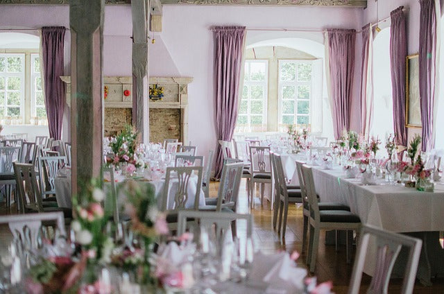 Salle de réception dressée pour un mariage, longues tables nappées et centres de table fleuris